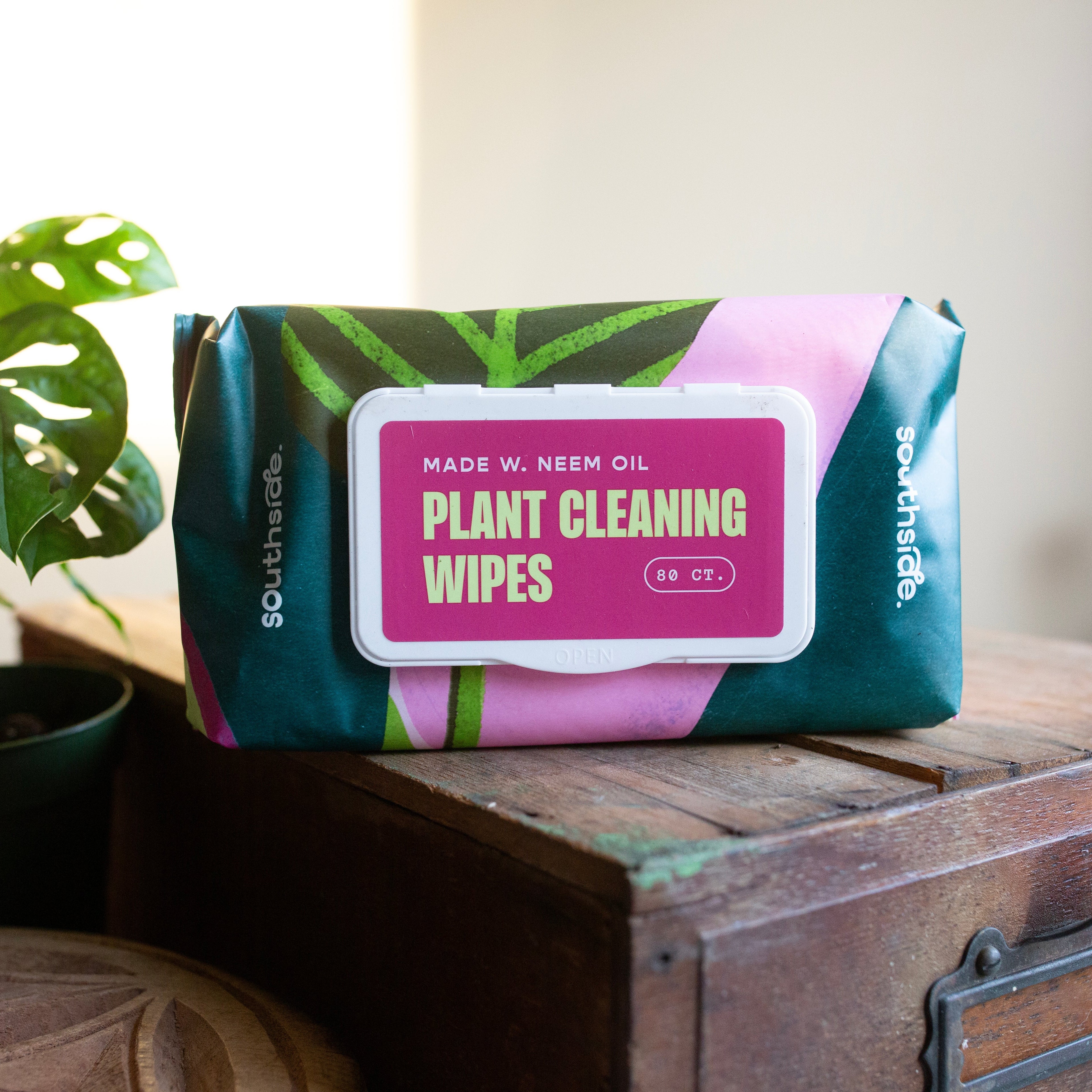 Plant cleaning wipes packaging on a wooden surface with plants in the background
