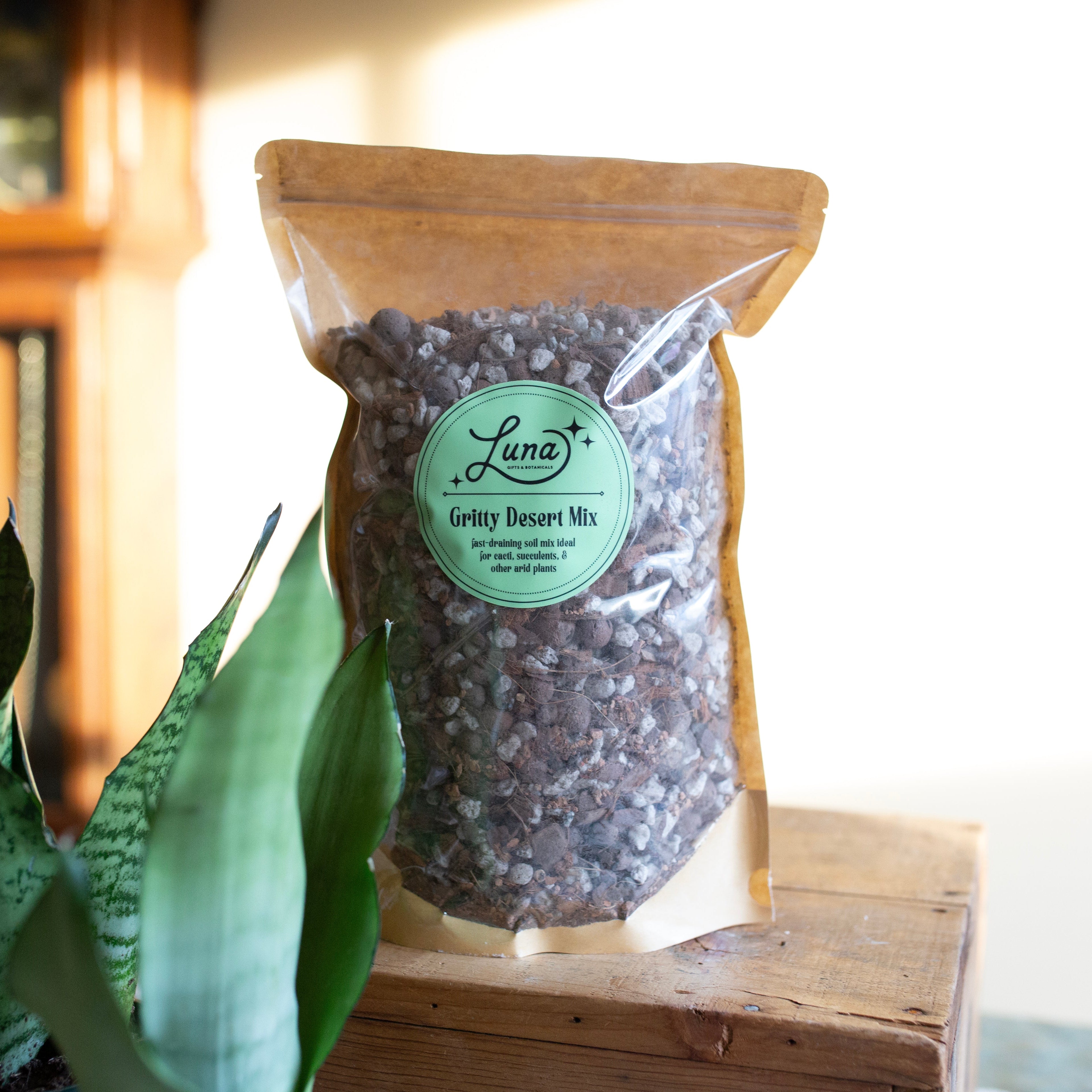 Bag of Luna's Gritty Desert Mix on a wooden surface with a plant in the foreground.