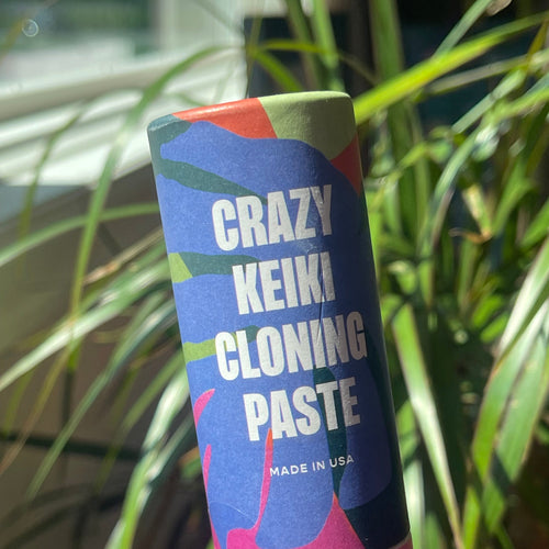 Crazy Keiki Cloning Paste container held by a hand with a plant in the background