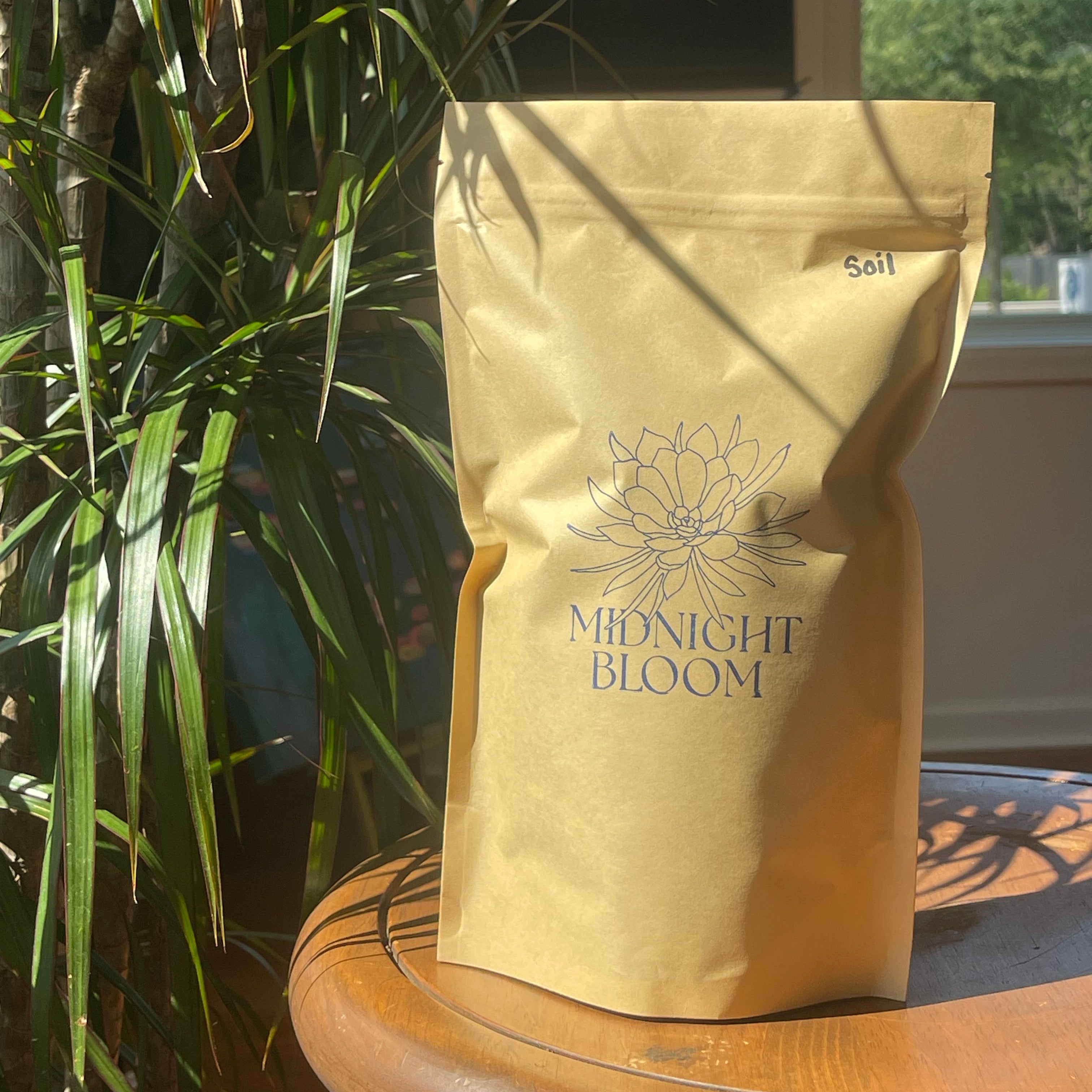 Brown package full of soil with Midnight Bloom stamped logo in front of a plant