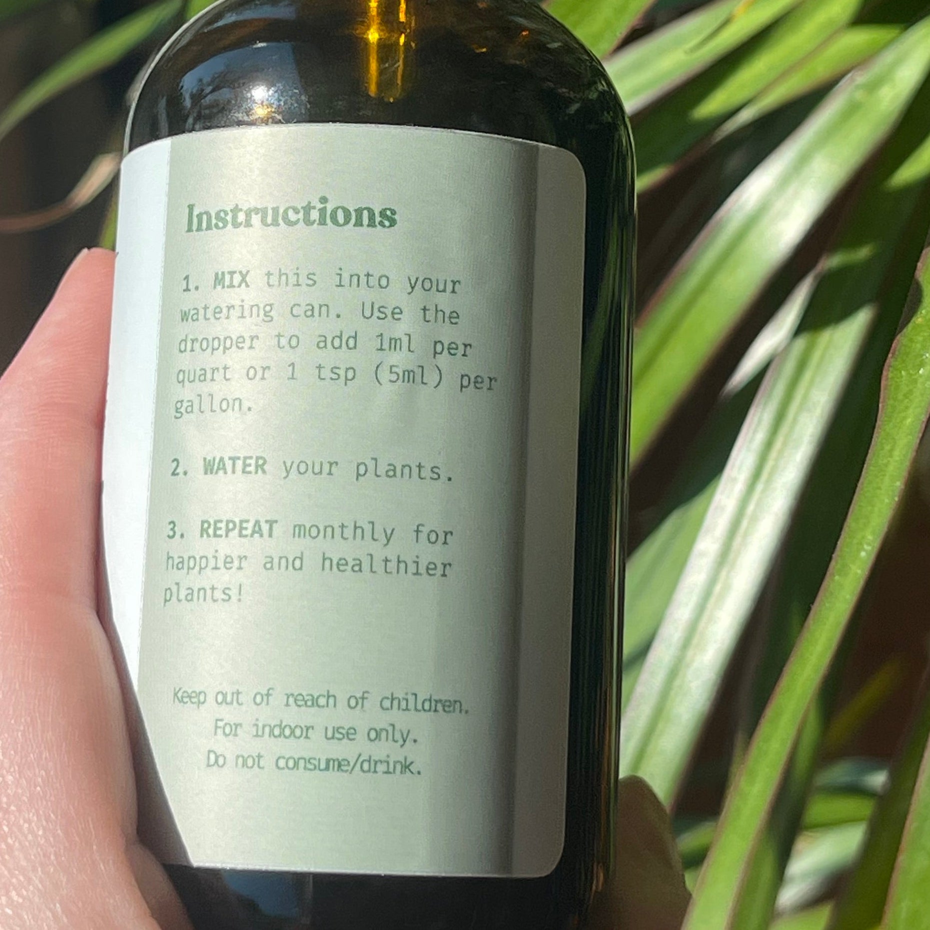 Hand holding a bottle with a label against a plant background