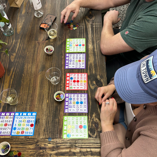 Two people playing a bingo with bingo cards on a wooden table.
